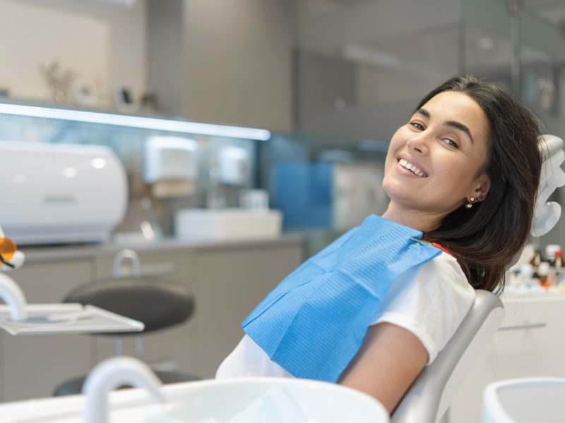 Pretty brunette happy female patient sitting in the chair at dental clinic